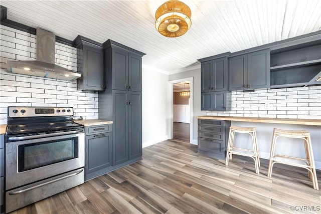 kitchen with tasteful backsplash, stainless steel range with electric cooktop, wall chimney range hood, and wood finished floors