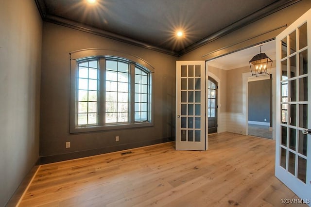 empty room featuring crown molding, wood finished floors, french doors, and a chandelier