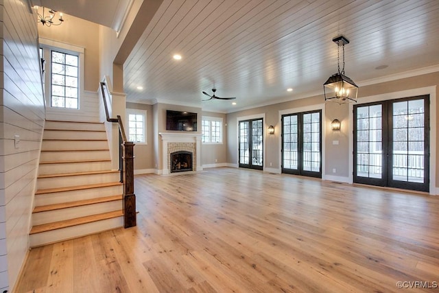 unfurnished living room with stairway, ornamental molding, french doors, a brick fireplace, and light wood-type flooring