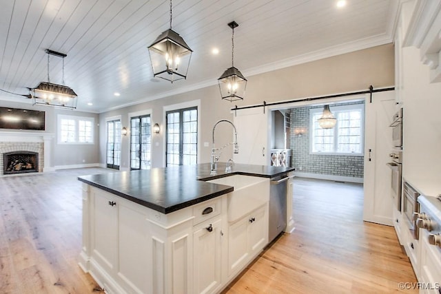 kitchen featuring dark countertops, light wood finished floors, a fireplace, ornamental molding, and a barn door