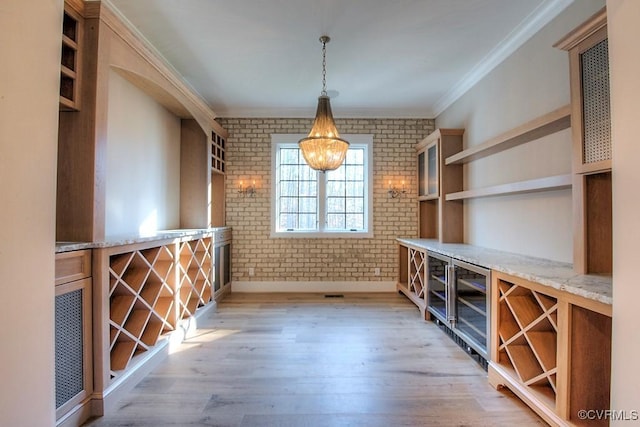 wine area featuring light wood-style flooring, brick wall, an inviting chandelier, and ornamental molding