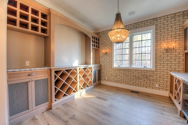 wine area with crown molding, a notable chandelier, light wood-type flooring, and brick wall