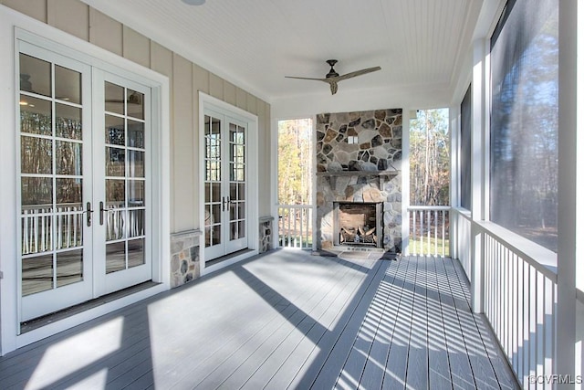 unfurnished sunroom with a wealth of natural light, french doors, a stone fireplace, and ceiling fan