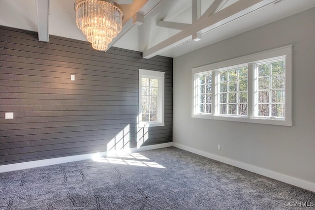 empty room with baseboards, carpet floors, beam ceiling, wood walls, and a chandelier