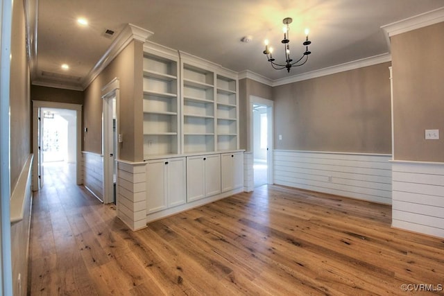 unfurnished dining area featuring a notable chandelier, hardwood / wood-style floors, wainscoting, and crown molding