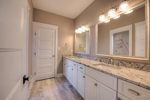 full bath featuring double vanity, wood finished floors, a tile shower, and a sink