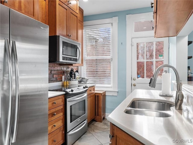 kitchen with light countertops, brown cabinetry, appliances with stainless steel finishes, and a sink