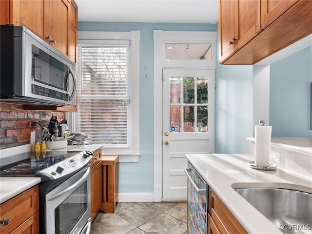 kitchen with light tile patterned flooring, brown cabinets, appliances with stainless steel finishes, and light countertops