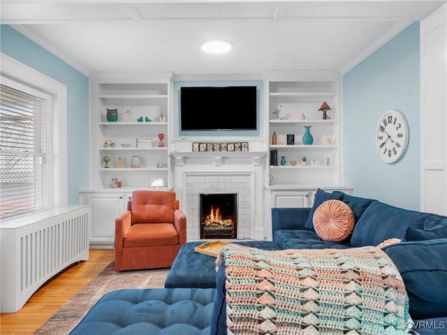 living room featuring light wood-type flooring, built in shelves, ornamental molding, radiator heating unit, and a brick fireplace