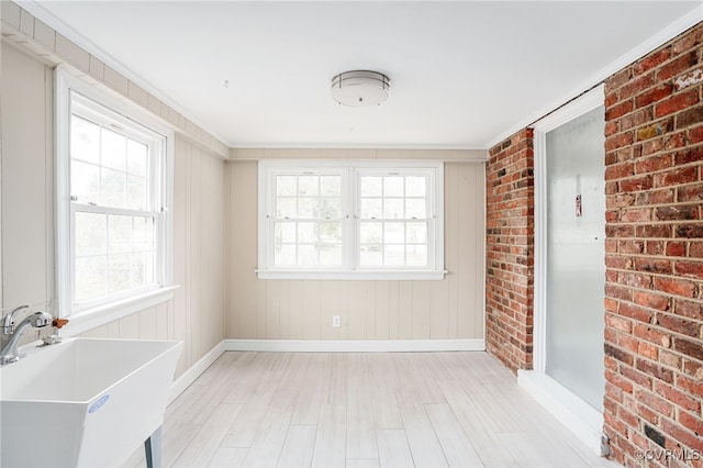 empty room with a sink, baseboards, brick wall, and light wood finished floors