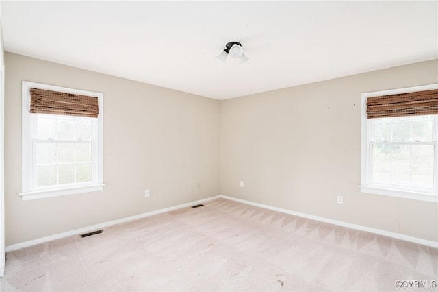 spare room with plenty of natural light, light colored carpet, baseboards, and visible vents