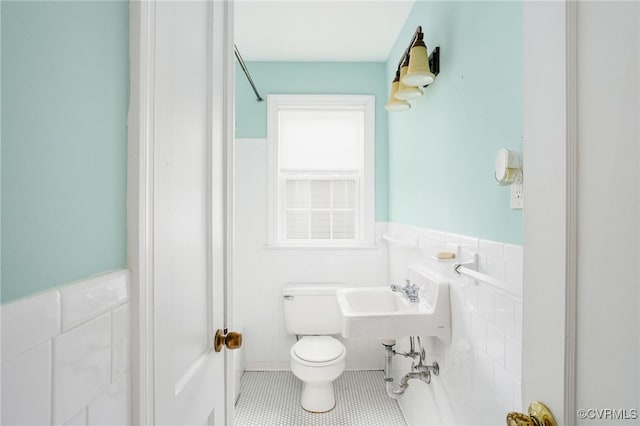 half bathroom with a wainscoted wall, toilet, a sink, tile walls, and tile patterned flooring