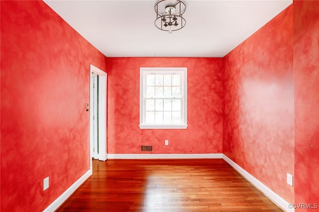 empty room featuring hardwood / wood-style floors, baseboards, and visible vents