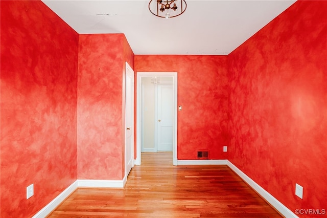 spare room featuring a notable chandelier, visible vents, baseboards, and wood finished floors