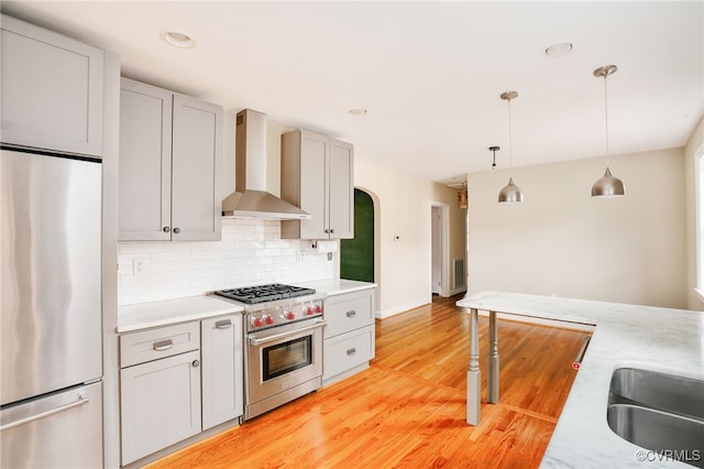 kitchen featuring light countertops, decorative backsplash, arched walkways, stainless steel appliances, and wall chimney exhaust hood