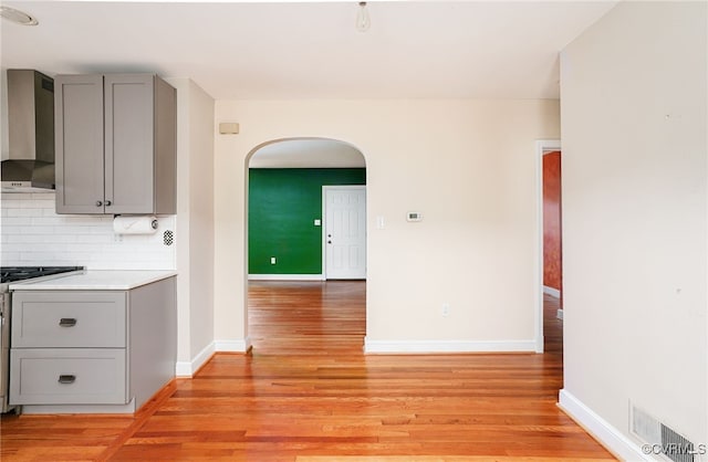 kitchen with visible vents, gray cabinets, backsplash, arched walkways, and wall chimney exhaust hood