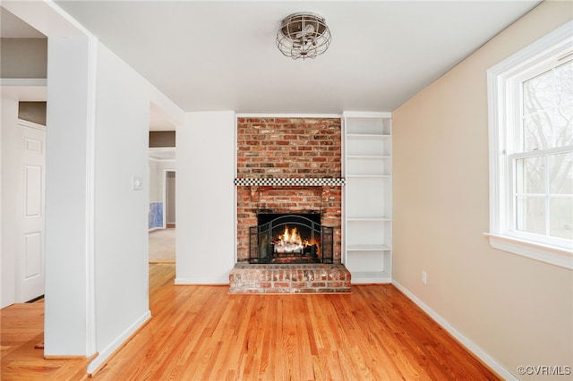 unfurnished living room featuring a fireplace, wood finished floors, a healthy amount of sunlight, and baseboards