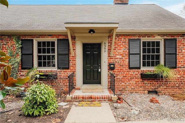 view of exterior entry featuring brick siding, a chimney, and a shingled roof