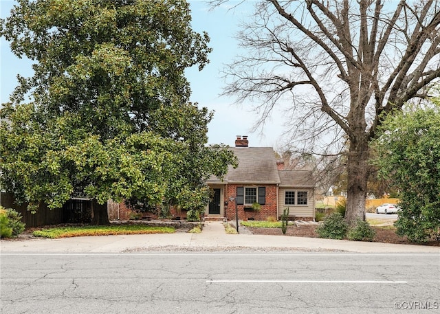 view of front of property featuring brick siding, fence, and a chimney