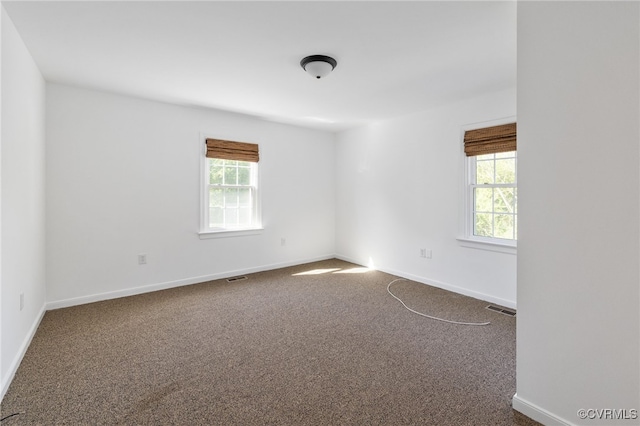 unfurnished room featuring baseboards, visible vents, a wealth of natural light, and dark colored carpet