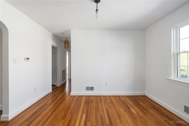 unfurnished room featuring arched walkways, visible vents, and wood finished floors