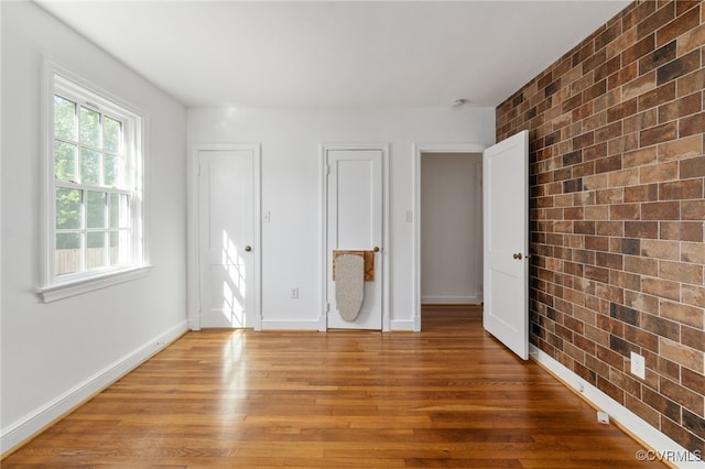 unfurnished bedroom with brick wall, baseboards, and light wood-style flooring
