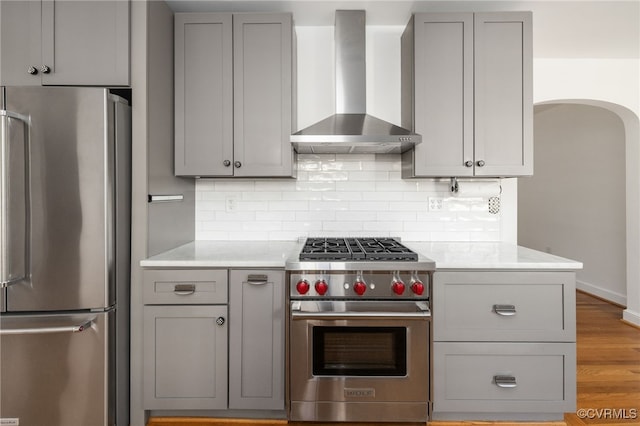 kitchen with gray cabinetry, appliances with stainless steel finishes, and wall chimney exhaust hood