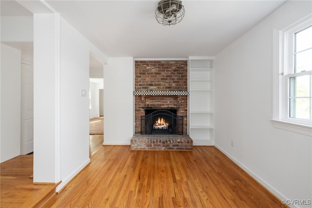 unfurnished living room featuring built in shelves, baseboards, a brick fireplace, and wood finished floors