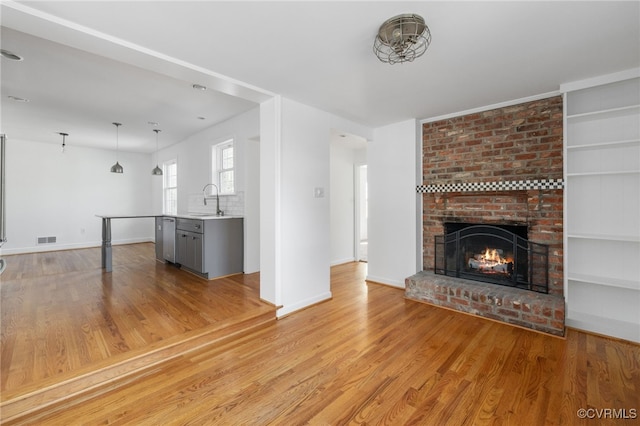 unfurnished living room with visible vents, a fireplace, light wood-type flooring, a sink, and baseboards