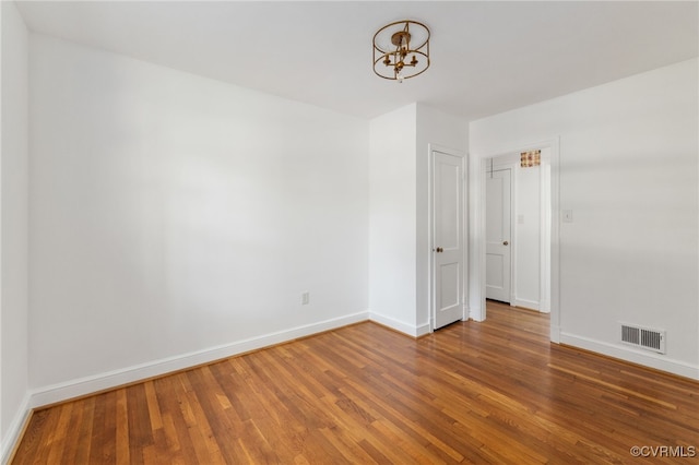 spare room with baseboards, a notable chandelier, visible vents, and wood finished floors