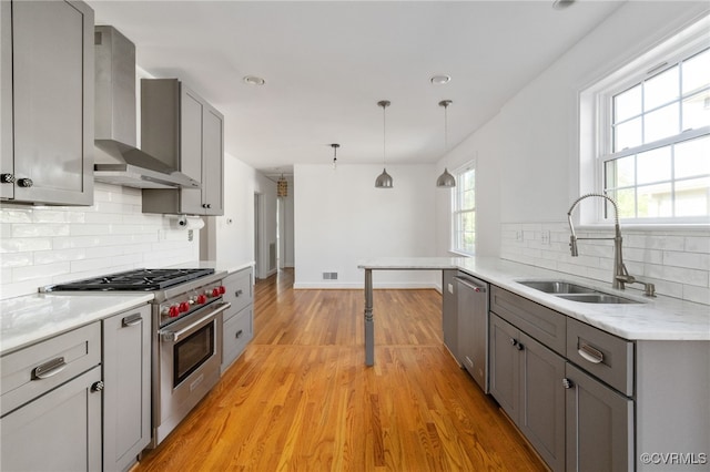 kitchen with a sink, light wood-style floors, wall chimney exhaust hood, stainless steel appliances, and gray cabinetry