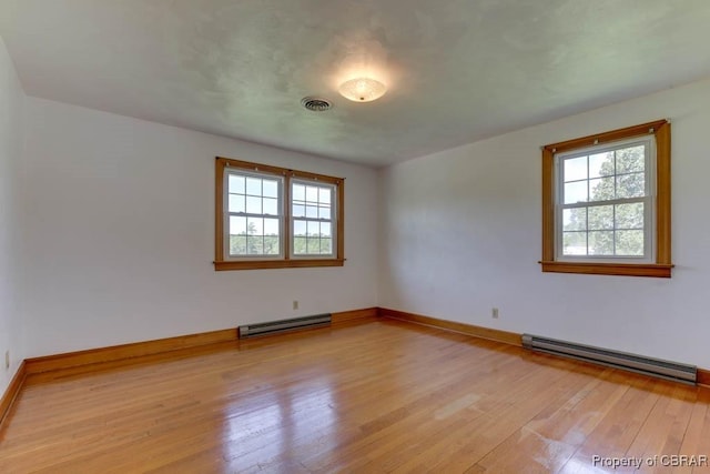 empty room featuring visible vents, light wood-type flooring, a baseboard heating unit, and baseboards