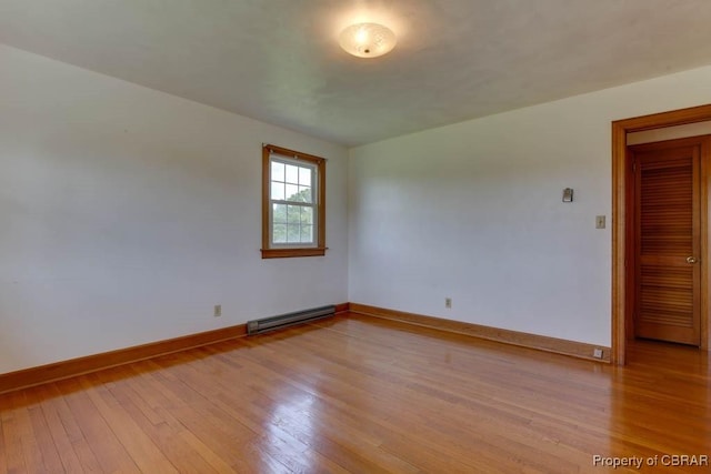 spare room featuring a baseboard heating unit, baseboards, and light wood finished floors