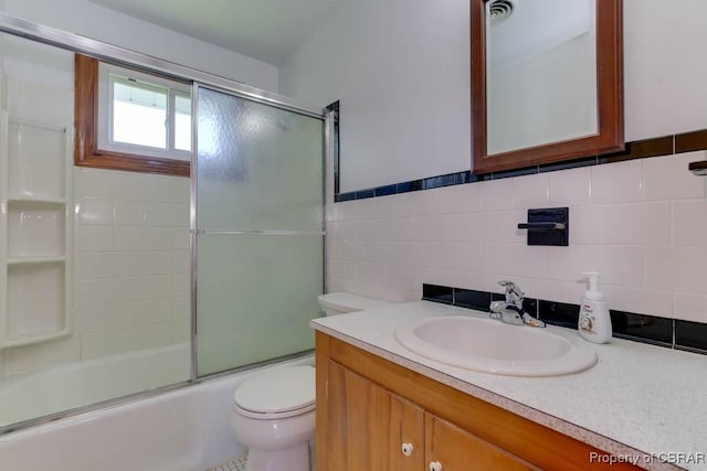 full bathroom featuring vanity, tile walls, toilet, and shower / bath combination with glass door