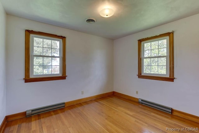 spare room featuring a baseboard heating unit, baseboards, visible vents, and light wood finished floors