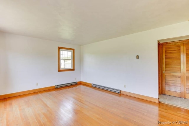 empty room featuring baseboards, a baseboard heating unit, and light wood-style floors