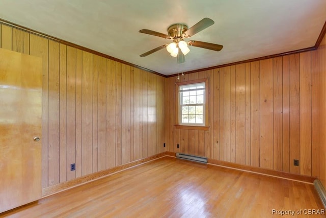 empty room featuring baseboard heating, crown molding, baseboards, and wood finished floors