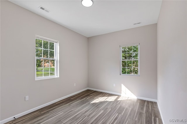 empty room featuring visible vents, plenty of natural light, wood finished floors, and baseboards