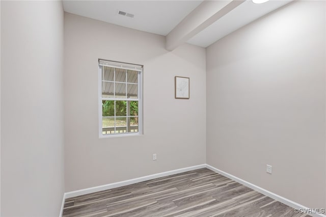 spare room featuring visible vents, baseboards, beam ceiling, and wood finished floors