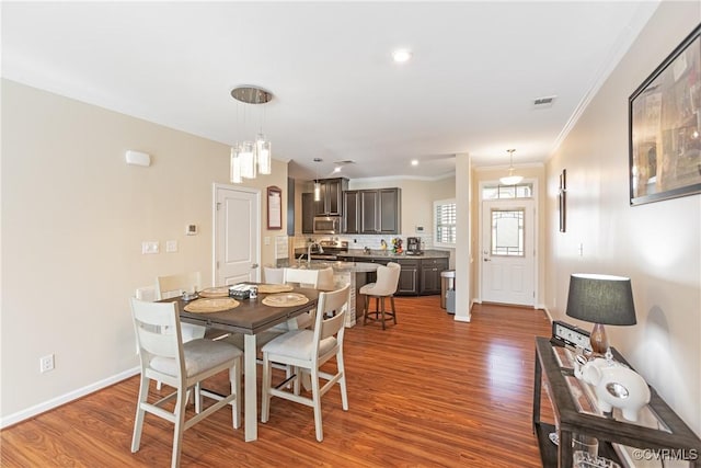 dining space featuring visible vents, ornamental molding, baseboards, and wood finished floors