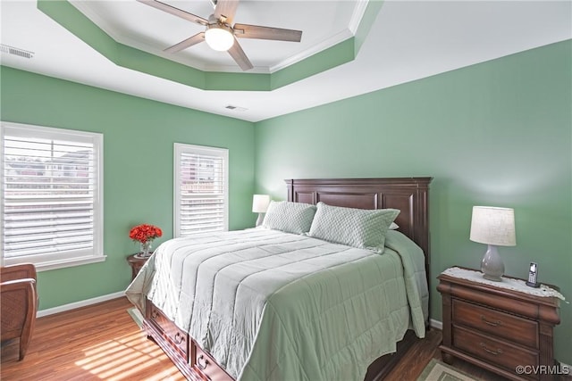 bedroom with a raised ceiling, wood finished floors, visible vents, and baseboards