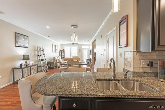 kitchen with wood finished floors, a peninsula, a sink, crown molding, and backsplash