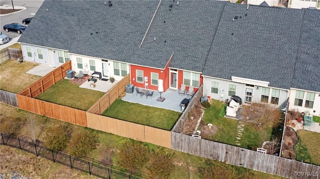 back of house featuring a fenced backyard, a residential view, a shingled roof, a patio area, and a lawn