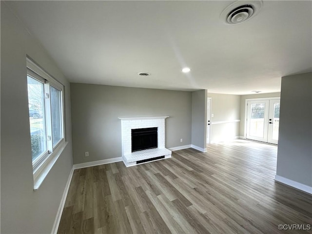 unfurnished living room featuring visible vents, a brick fireplace, baseboards, and wood finished floors