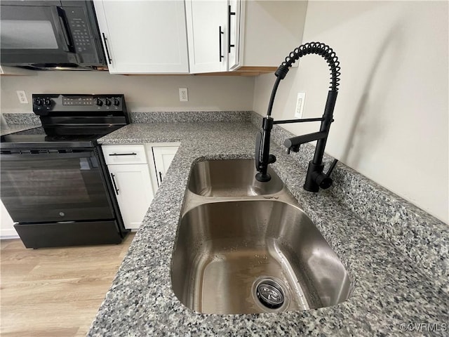 details with black appliances, white cabinets, light wood finished floors, and a sink