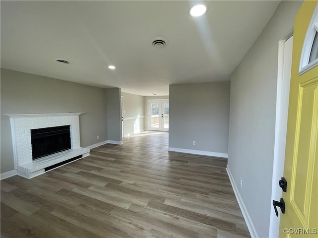 unfurnished living room featuring visible vents, a brick fireplace, baseboards, and wood finished floors