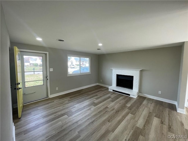 unfurnished living room with visible vents, wood finished floors, recessed lighting, baseboards, and a brick fireplace