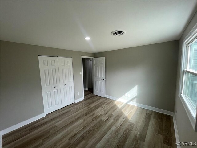 unfurnished bedroom with visible vents, baseboards, a closet, and wood finished floors