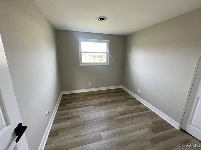 empty room featuring wood finished floors, visible vents, and baseboards