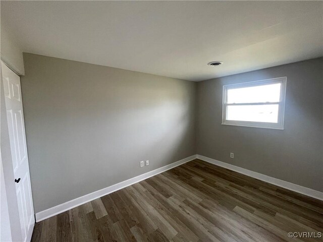 spare room featuring dark wood finished floors, visible vents, and baseboards